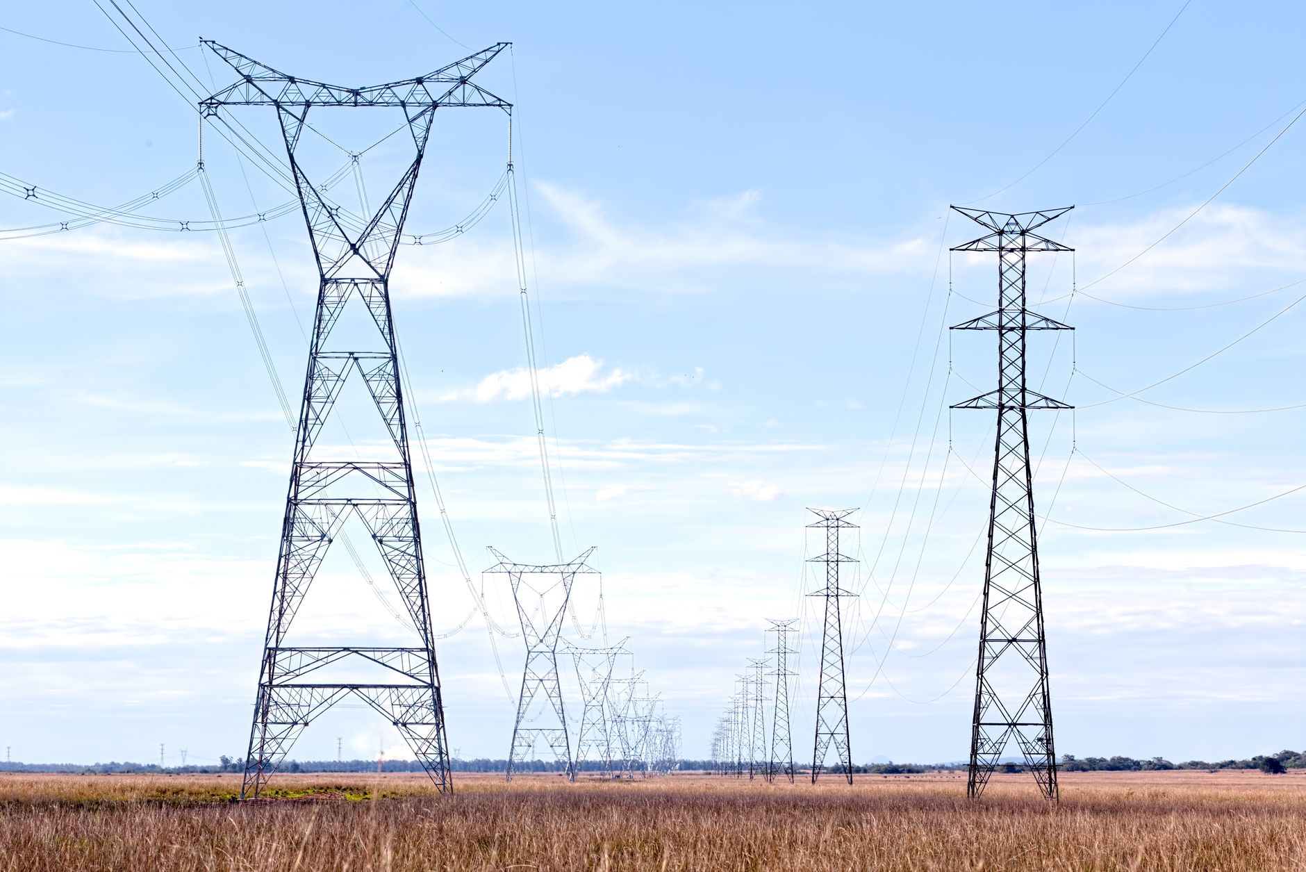 High voltage pylons stretching across a vast open field under a clear blue sky