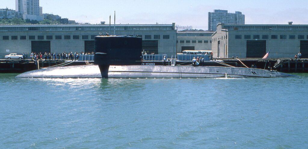 A naval submarine docked at an urban harbor