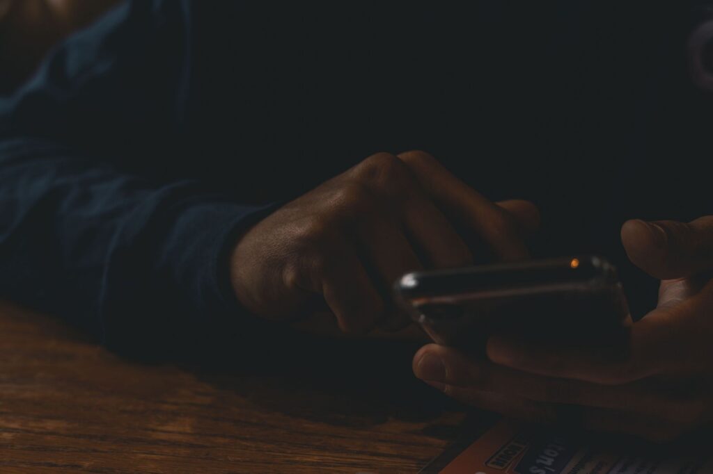 Close-up of hands interacting with a smartphone in a dim indoor setting