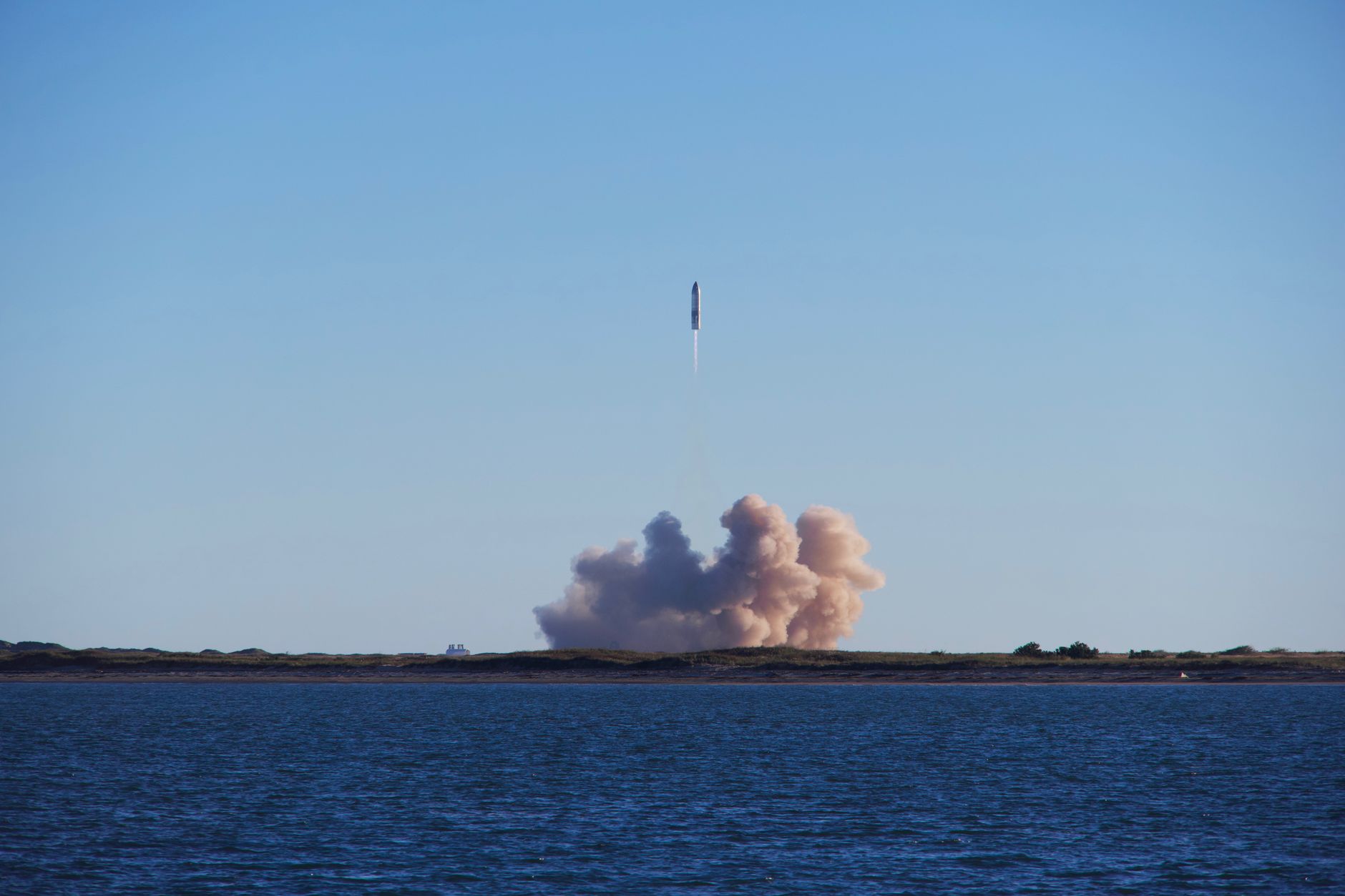 A rocket rising on a column of smoke over the water at dawn