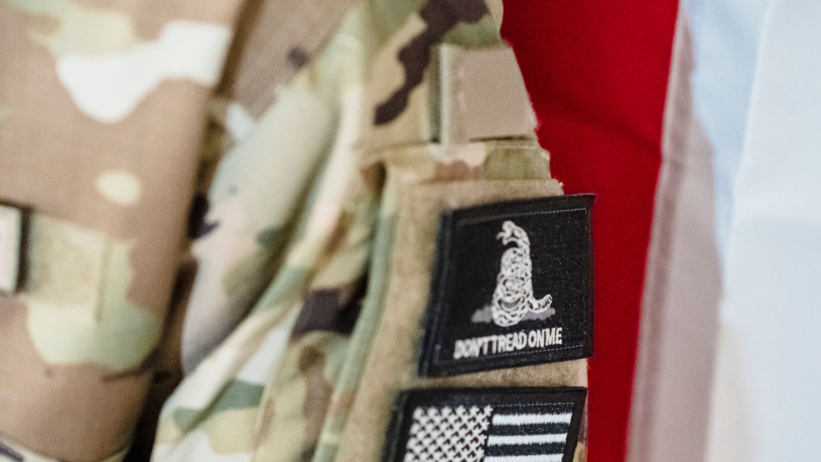Close-up of a U.S. military camouflage uniform with unit patches in front of an American flag