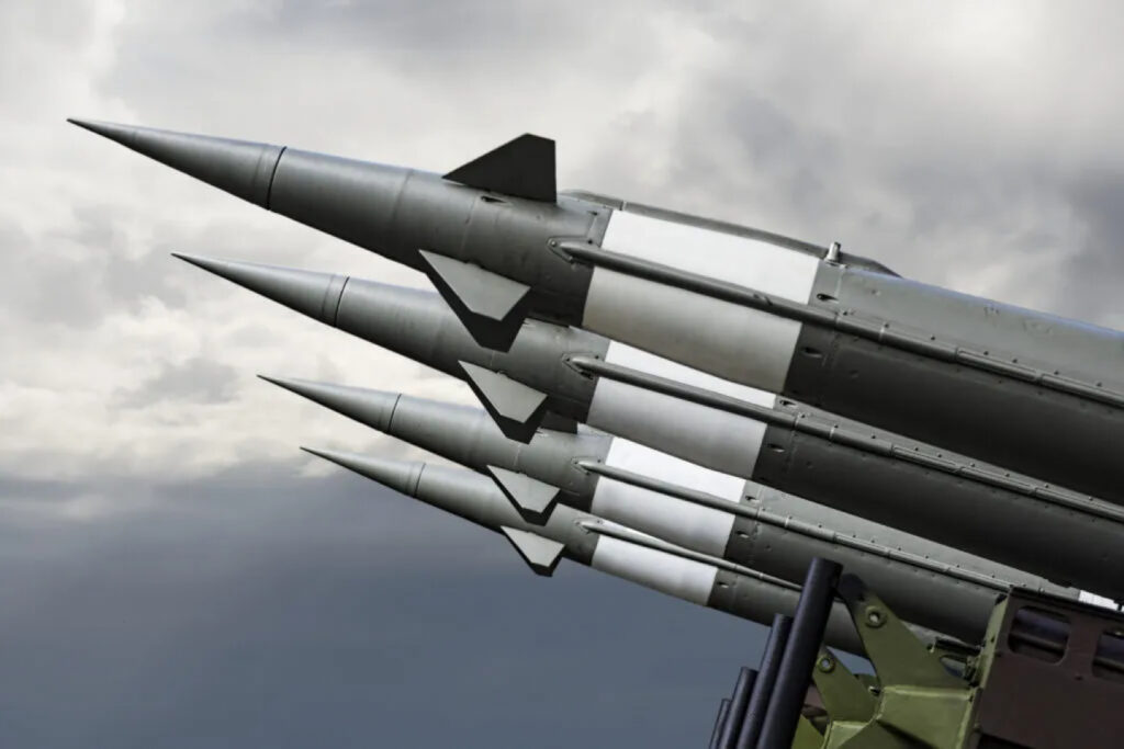 A row of four missiles angled skyward on a launcher against an overcast sky.