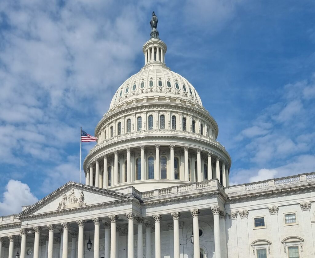 The US Capitol dome with the American flag against a blue sky in Washington, DC