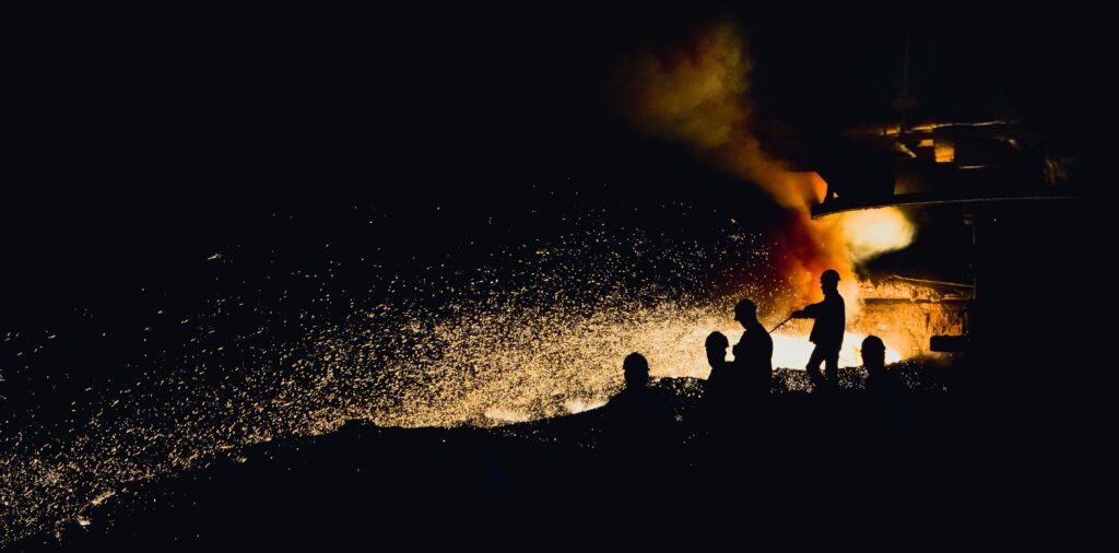 Foundry workers silhouetted against sparks and molten metal