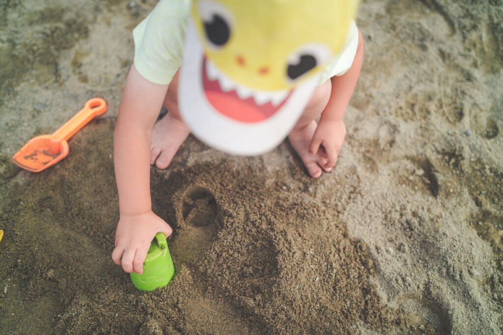 A young child playing in the sand with beach toys on a sunny day