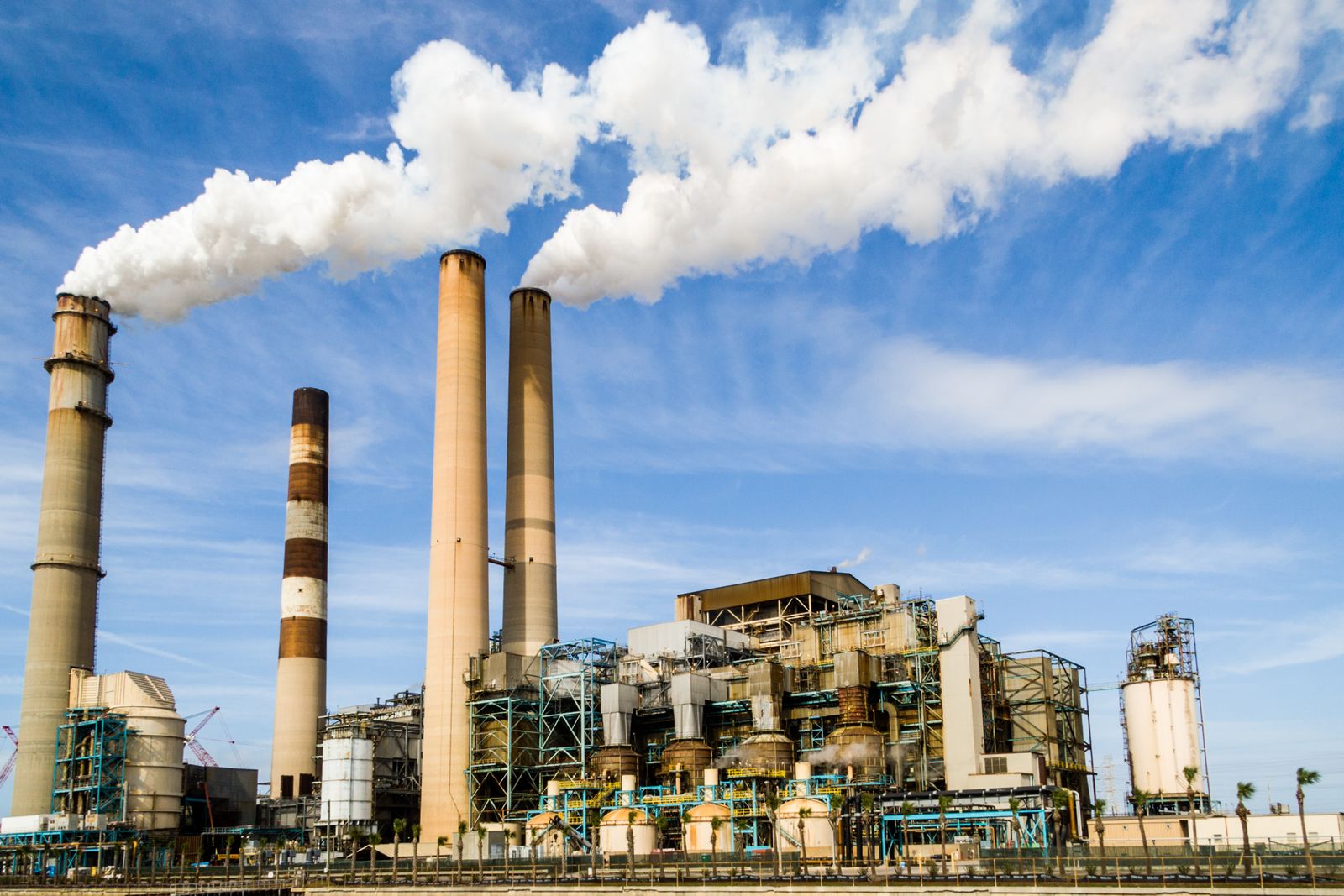 An industrial power plant with smokestacks emitting steam against a blue sky