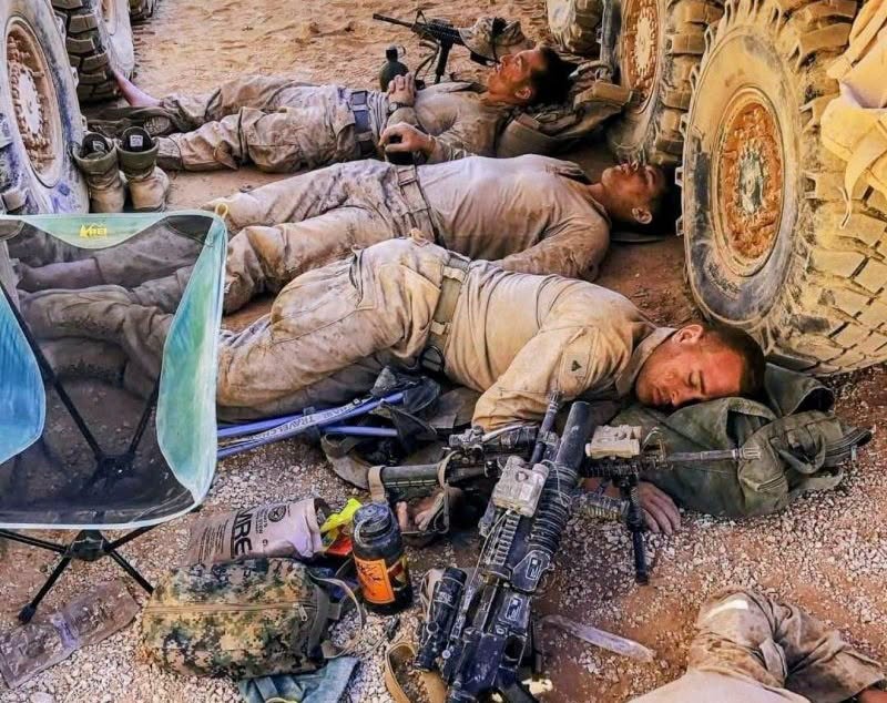 Exhausted Marines asleep on the ground beside a military vehicle's tires, rifles at their side
