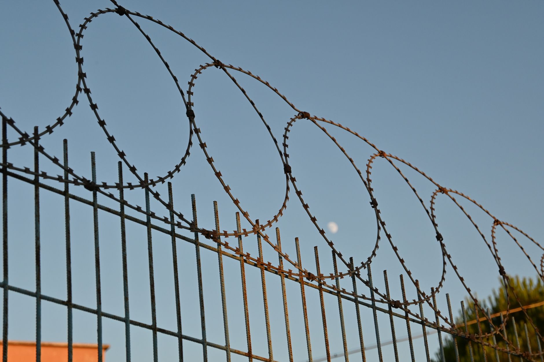 A barbed wire fence under a clear blue sky. Photo by Hilal on Pexels